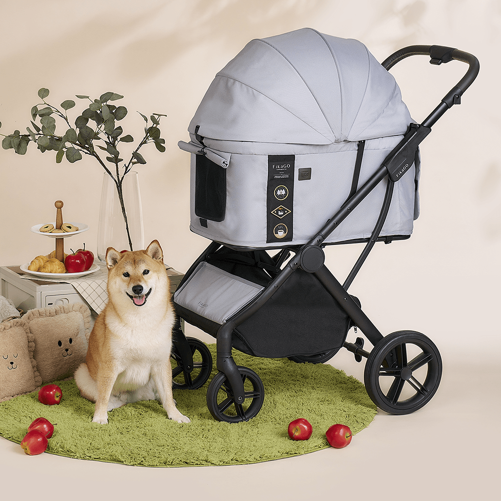 A dog is sitting beside the FikaGO AGILE 2 pet stroller in soft grey